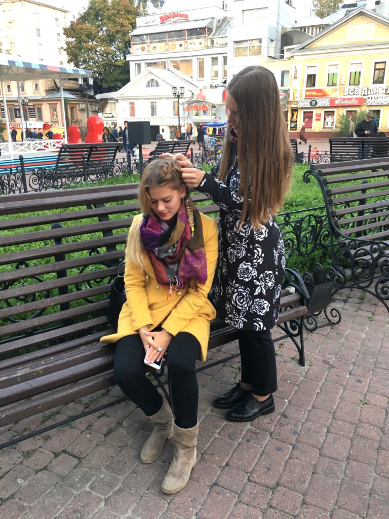 Uma jovem russa arruma o cabelo da amiga em uma pracinha. Observe que uma delas segura um iPhone em suas mãos